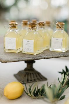 several bottles of lemonade sit on a tray next to two lemons and an olive branch