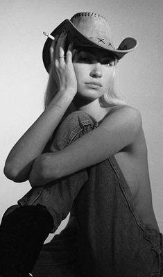 a black and white photo of a woman wearing a cowboy hat with her hands on her head