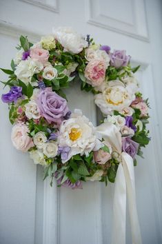 a wreath is hanging on the door with white and purple flowers around it, along with a bow