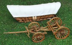 an old wooden wagon with two wheels and a blanket on the back sits in grass