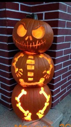 three pumpkins stacked on top of each other in front of a brick wall with glowing eyes