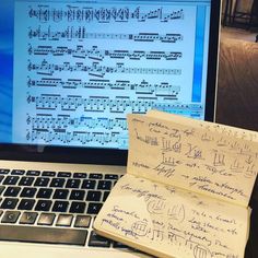 an open notebook sitting in front of a laptop computer with music notes on the screen