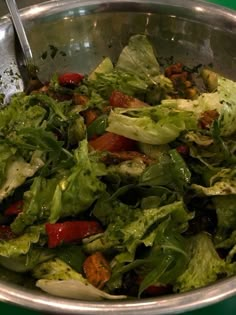 a salad with lettuce, tomatoes and other vegetables in a silver bowl on a green table