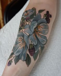 a woman's arm with blue flowers and berries on the inside of her leg