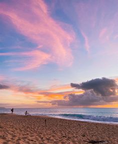 two people are walking on the beach with their surfboards under a colorful sky at sunset