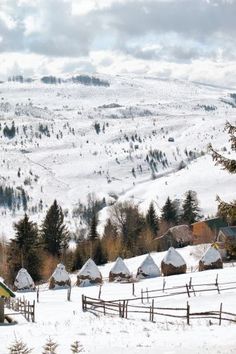 a snowy landscape with houses and trees in the foreground, surrounded by snow covered hills