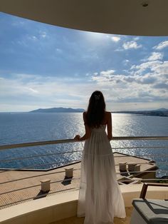 a woman in a white dress looking out over the ocean from a balcony with chairs