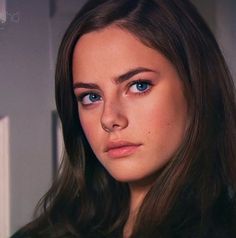 a woman with long hair and blue eyes looks at the camera while standing in front of a door