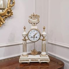 a white and gold clock sitting on top of a wooden table next to a mirror