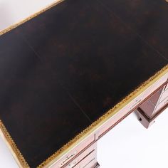 an antique desk with gold trimmings and black leather on the top, sitting against a white background