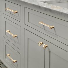 a kitchen with marble counter tops and gold handles on the drawers in front of the sink