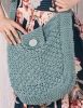 a person holding up a blue crocheted sweater with a button on the front