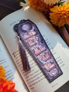 an open book with a tassel on top of it and flowers in the background