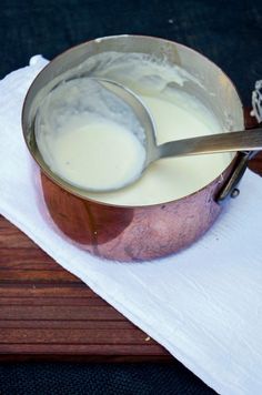 a spoon is in a bowl of milk on a napkin with a wooden board behind it