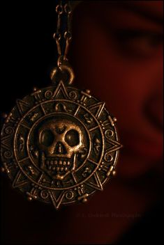 a person wearing a gold necklace with a skull on the front and an ornate design on the back