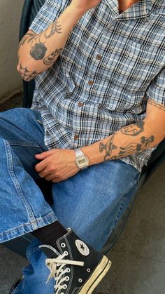 a man with tattoos sitting on a chair talking on a cell phone and holding his hand up to his ear