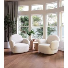 two white chairs sitting next to each other on top of a hard wood floor in front of large windows