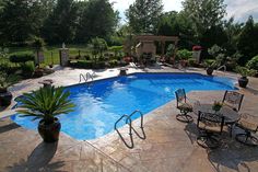 an empty swimming pool surrounded by patio furniture and landscaping area with potted plants on either side