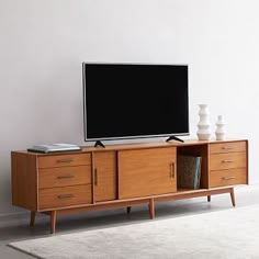 a flat screen tv sitting on top of a wooden entertainment center next to a white rug