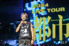 a man standing in front of a large screen with the words live tour written on it