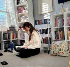 a young woman sitting on the floor in front of a book shelf filled with books