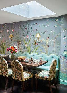 the dining room is decorated with floral wallpaper and blue velvet upholstered chairs