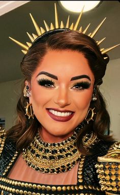 a woman wearing gold and black makeup with spikes on her head, smiling at the camera