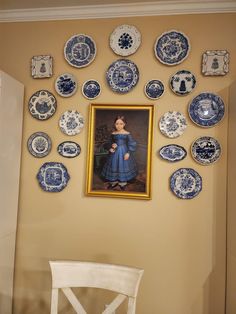 a painting on the wall with blue and white plates arranged around it in front of a chair