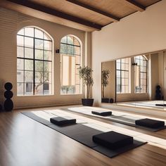 there are many yoga mats on the floor in front of two large windows with potted plants