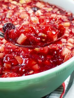 a spoon full of cranberry sauce in a green casserole dish on a striped cloth