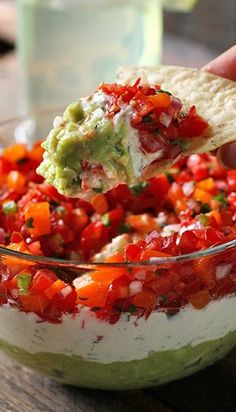 a person dipping guacamole into a bowl with tortilla chips on the side