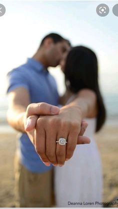 a man and woman are holding hands on the beach with their engagement ring in front of them