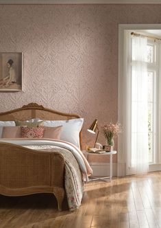 a bedroom with pink walls and wood flooring has a wicker bed frame, white pillows, and decorative artwork on the wall