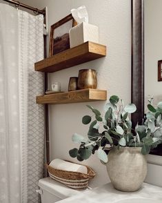 a white toilet sitting under a bathroom mirror next to a wooden shelf filled with items