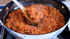 a large pot filled with food cooking on top of a gas burner next to a wooden spoon