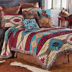 a bed covered in colorful blankets and pillows next to a brown cowhide rug on a wooden floor