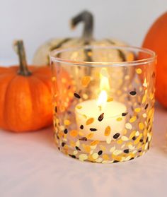 a lit candle sits in front of some pumpkins