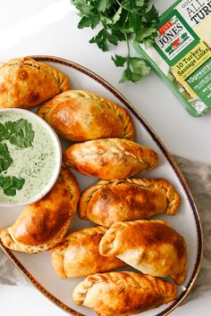 several pastries on a plate with a bowl of dip and parsley next to it