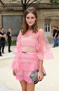 a woman standing in front of a building wearing a pink dress and holding a purse