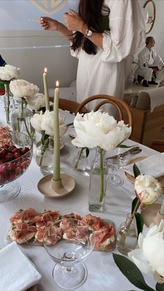 a woman standing in front of a table filled with food and flowers on top of it