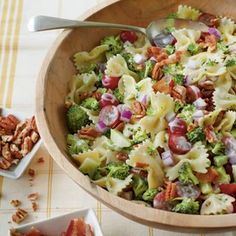 a wooden bowl filled with pasta salad next to two small bowls full of nuts and broccoli