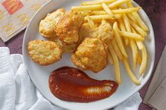 a white plate topped with fried food next to french fries and ketchup on a table