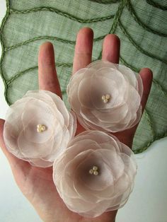 three small flowers are held in the palm of someone's hand, with pearls on them