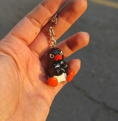 a hand holding a small keychain with a penguin on it's face