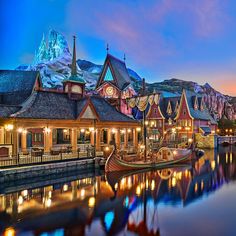 a boat is docked in the water near buildings and mountains at night with lights on them