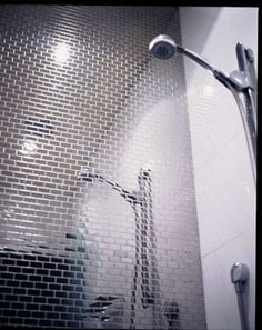 a shower head and hand held shower faucet in a white tiled bathroom area