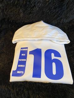 a white and blue shirt with the number sixteen on it is laying on black fur