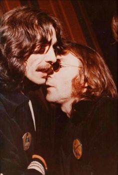 two men are kissing each other while one is wearing sunglasses and the other has long hair