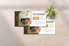 two gift voucher cards sitting on top of a wooden table next to a plant