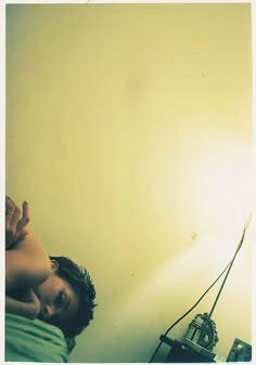 a young man laying in bed with his hand up to the ceiling and light shining on him